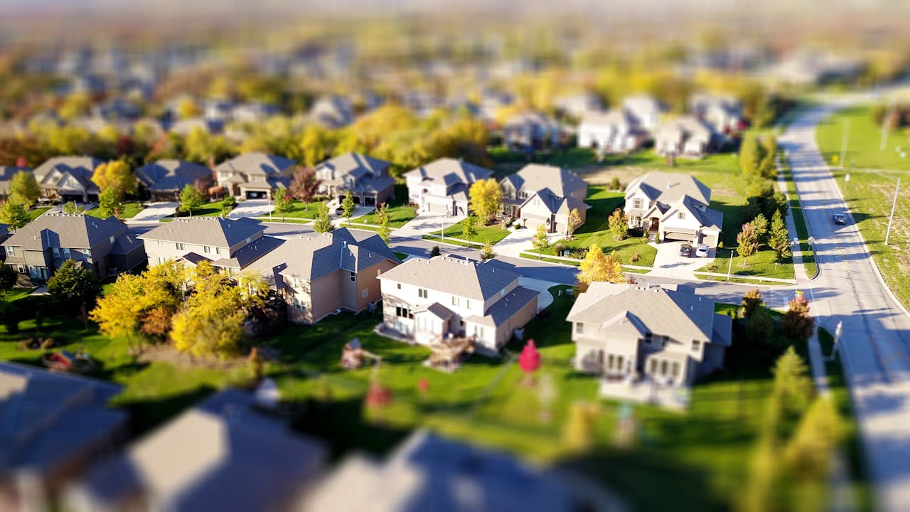 about-01 Tilt-shift aerial photo of a suburban neighborhood with green lawns and roads.