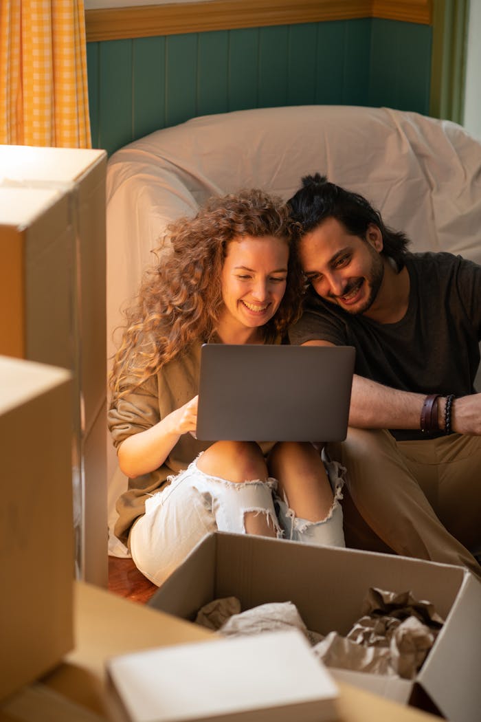 services-img Smiling couple using laptop while unpacking boxes in their new home. Bright, cozy indoor setting perfect for relocation themes.